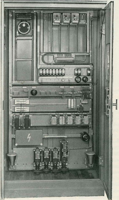 Schaltschrank mit geöffneten Türen, oben links ein Motorrelais, oben rechts vier Kleinrelais-Steckplätze, auf denen drei Relais eingesetzt sind, in der Mitte Sicherungen, darunter Selen-Gleichrichter, Kondensatoren und Transformatoren, unten Kabelendverschlüsse