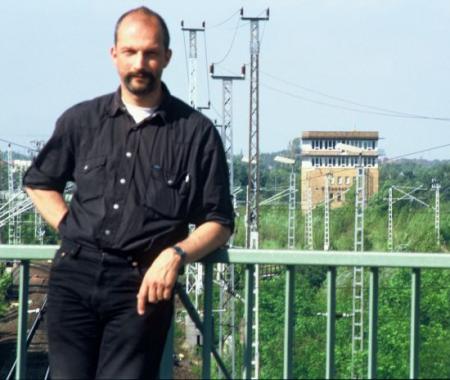 Foto: Steffen Buhr auf einer Brücke am Geländer, im Hintergrund Gleise, Oberleitungsmaste und das Stellwerk Grünauer Kreuz